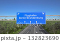 Blue motorway sign for Berlin Brandenburg Airport with an airliner flying above along the road toward the airport 132823690