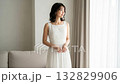 A woman in a white dress standing by the window looking outside 132829906