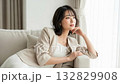 A woman sitting on a sofa, resting her chin on her hand and smiling gently 132829908