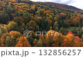 Aerial view of small wooden cabin surrounded by vibrant autumn forest. Peaceful fall mountain landscape with colorful foliage, cozy atmosphere, and scenic natural beauty. 132856257