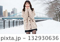 A woman in a knitted sweater and skirt raising one leg on a snowy riverbank 132930636