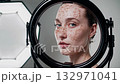 Woman with natural freckles looking at her repeated reflection in several round makeup mirrors, presenting a beauty concept in a studio setting with softbox lights 132971041