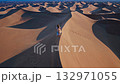 Morning stroll over desert terrain, Aerial footage showing woman crossing sandy hills at dawn, Early morning landscape shot of woman walking amidst expansive desert sand dunes with cinematic 132971055