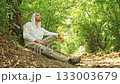 A hiker rests on the side of a trail in the forest on a hot summer day 133003679