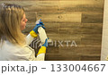 Woman cleans in the bathroom and washes a wall of tiles with detergent on a brown background. 133004667