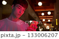 Young Stylish Guy Wearing White T-Shirt Using his Smartphone to Chatting in Social Networks Standing at Futuristic Neon Club Lights Background. Close Up 133006207