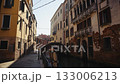 Picturesque Venetian street with water canal and footbridge capturing medieval atmosphere. Ancient apartment buildings on waterway banks in old Italian city district. Medieval town 133006213