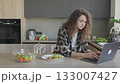 Woman Working On Laptop While Eating Healthy Salad In Modern Kitchen 133007427