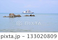 Ferry ship sailing on calm sea with rocks in the foreground under clear blue sky 133020809