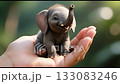 A playful baby elephant in a palm, trunk lifted happily as sunlight glows behind, symbolizing wonder, happiness, and connection with nature. 133083246