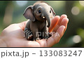 A cute baby elephant sitting in a hand, gazing upward with big expressive eyes, showcasing innocence, joy, and love for animals. 133083247