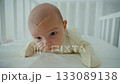A small one-month-old baby is lying on its stomach in a crib and trying to lift its head. The concept of children's development 133089138