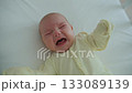 A one-month-old baby lies in a wooden crib, kicking and crying 133089139