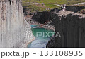 Studlagil Canyon in Iceland features basalt columns, a turquoise river, and visitors walking, climbing, and exploring the lush green surroundings. 133108935