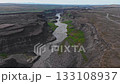 Aerial view of Studlagil Canyon in Iceland, showcasing basalt columns, a winding river, green vegetation, and steady camera movement along the terrain. 133108937