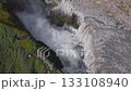 Aerial perspective of Dettifoss waterfall in Iceland, with powerful water currents plunging into a misty canyon surrounded by rugged rocky terrain. 133108940
