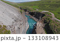 Aerial view of Studlagil Canyon in Iceland, featuring basalt columns, a turquoise river, and visitors walking along the canyon's edge and rocky paths. 133108943