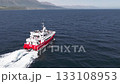 Aerial view of the Holmasol whale watching boat navigating calm waters near Iceland's coast, with passengers and scenic hills in the background. 133108953