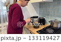 Young woman pouring tea with honey from teapot into cup in kitchen 133119427