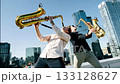 Two saxophonists play a duet on the roof of a high-rise building in the business district of a large city. 133128627