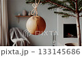 Close-up of a simple wooden Christmas ornament on a minimalist fir tree. Blurred Scandinavian interior with fireplace and natural daylight creates a serene, eco-friendly holiday atmosphere. 133145686