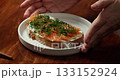 Top view on Sandwich with red fish. The chef rotation the plate in camera on which lies a salmon sandwich sprinkled with fresh dill, preparing a homemade appetizer. 133152924