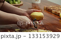 Close up of hands peeling fresh potato with peeler on wooden table, preparing ingredients for homemade vegan meal, cooking process, healthy food, rustic kitchen atmosphere, natural lifestyle 133153929