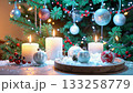 Glowing candles on fake snow with ornaments and festive christmas tree. 133258779