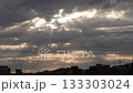 Dramatic sky with dark clouds and rays of sunlight breaking through. Urban skyline silhouette at dusk. Atmospheric and moody scene. 133303024