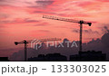 Silhouettes of construction cranes against a vibrant sunset sky. The scene captures the essence of urban development and industrial growth. 133303025
