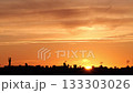 A vibrant sunset over a city skyline. The sky is filled with orange and yellow hues, silhouetting buildings and antennas against the colorful backdrop. 133303026