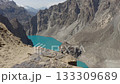 Aerial view of a breathtaking turquoise lake nestled in the rugged mountains of Pakistan, highlighting a woman in stark contrast between the vibrant water and the barren landscape 133309689