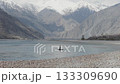 A solitary rower navigates a tranquil river amidst towering snow-capped mountains in Pakistan 133309690