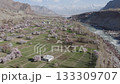 Aerial view of a serene village in the mountains of Pakistan, surrounded by lush orchards and a flowing river 133309707