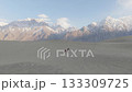 Aerial view of a solitary horse rider traversing the vast desert sands of Pakistan, with majestic snow-capped mountains rising in the background 133309725