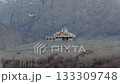 Aerial view of a white building with a green dome nestled in the mountains of Pakistan, showcasing traditional architecture and a majestic snow-capped peak in the background 133309748