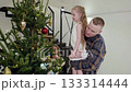 Happy family decorating christmas tree at home, father holding daughter helping her to put ornaments on the tree, mother decorating the tree too 133314444