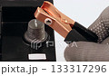 Close-up of a copper jumper cable clamp being connected to a car battery terminal by a gloved hand for electrical maintenance 133317296