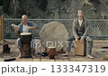 A man performs ritual music on ethnic percussion instruments by a glowing campfire under the night. 133347319