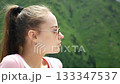 Young woman in sunglasses looking at green mountains outdoors in summer 133347537