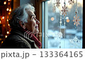 Elderly woman gazes thoughtfully out the window, observing snowflakes and winter scenery, with a gradual camera zoom enhancing emotional connection 133364165