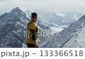 Man in yellow shirt gazes at majestic snow-capped mountains, camera pans 133366518