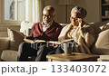 Elderly African American couple sits on sofa reading books and drinking coffee in sunlight. This cozy scene of retirement and love is perfect for lifestyle ads. 133403072