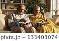 Elderly Indian couple sits on sofa reading books in sunlit living room. Peaceful scene portrays retirement leisure, lifelong learning, and domestic happiness for lifestyle content. 133403074