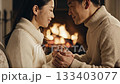 Close up of happy Asian couple touching foreheads and holding hands by a fireplace. Cozy romantic winter scene perfect for holiday or relationship concepts. 133403077