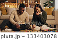 Cheerful interracial couple sitting on floor playing board game in cozy living room. Scene depicts happy evening leisure and togetherness. Ideal for lifestyle and relationship concepts. 133403078