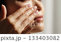 Close up of young woman applying white moisturizer cream to cheek. Concept of daily skincare routine and beauty hygiene. Perfect for dermatology ads, spa promotion and beauty blogs. 133403082