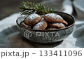 A rustic bowl of gingerbread cookie covered with powdered sugar and pine twig decoration on linen fabric in warm natural light 133411096