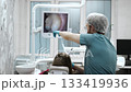 Dentist explaining tooth condition to patient on screen during oral exam. 133419936