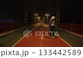 A stylish, fashionable girl dances a modern dance, at night in winter, cold autumn, on a bridge, against the background of a big city, river, road, cars, under the light of lanterns, lights. 133442589